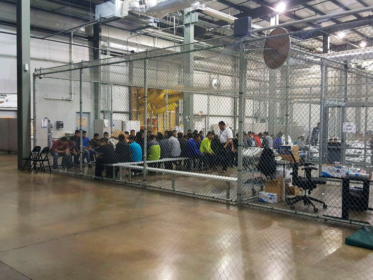 People sit on benches inside a cage in the facility