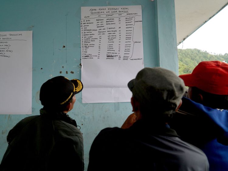 Family members look at a survivor list at the Lake Toba ferry port 